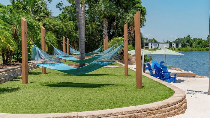 Tranquil waterfront oasis with inviting blue hammocks and Adirondack chairs under striped umbrellas, perfect for relaxation.