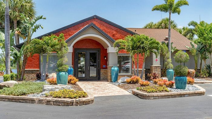 Inviting apartment entrance with vibrant landscaping, tropical greenery, and elegant blue planters.