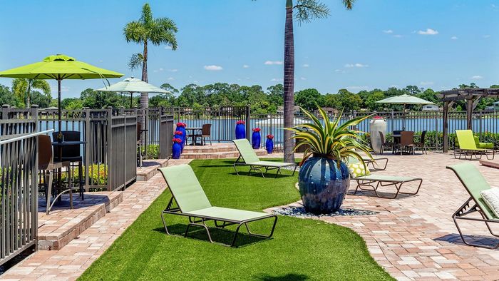 Charming outdoor patio with scenic lake views, featuring lounging chairs, vibrant green umbrellas, and lush palm trees, perfect for relaxation and entertaining.