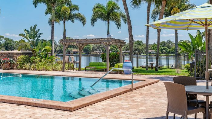 Luxurious poolside retreat featuring a sparkling blue swimming pool, lush landscaping, and serene lake views under sunny skies.