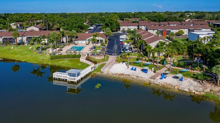 Idyllic waterfront apartment complex with lush greenery, a sparkling pool, and a charming dock extending into the tranquil lake.
