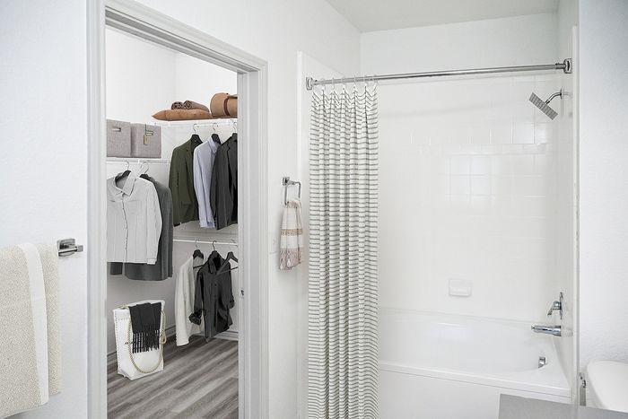 Elegant bathroom with a modern tub and stylish striped shower curtain, adjacent to a spacious walk-in closet showcasing neatly organized shelves and clothing racks.
