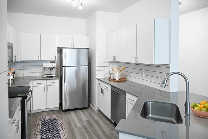 Modern kitchen with sleek gray countertops, stainless steel appliances, white cabinetry, and stylish backsplash.