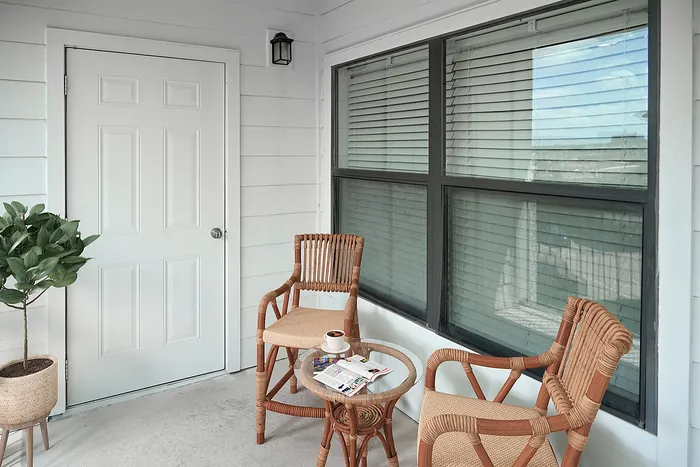 Charming patio space with cozy wicker chairs and lush plant, ideal for relaxing with a cup of coffee.