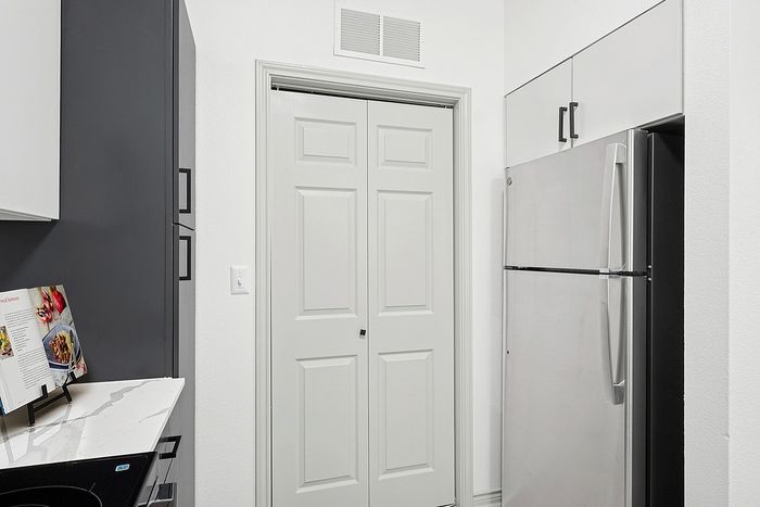 Modern kitchen corner showcasing a sleek stainless steel refrigerator, elegant white cabinetry, and a stylish marble countertop.