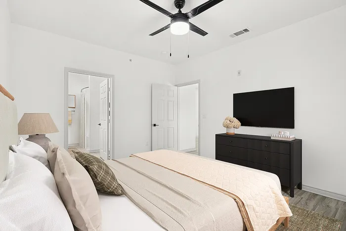 Modern bedroom with inviting beige tones, flat-screen TV, stylish dresser, and ceiling fan.