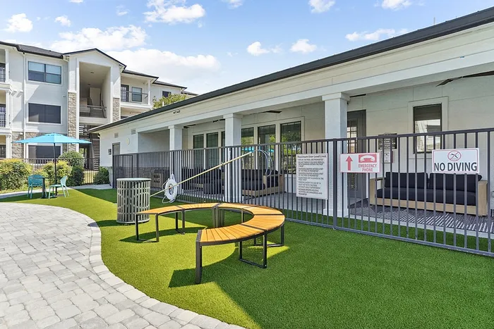 Inviting communal space with outdoor seating, lush green lawn, and sunny poolside relaxation area in a modern apartment complex.