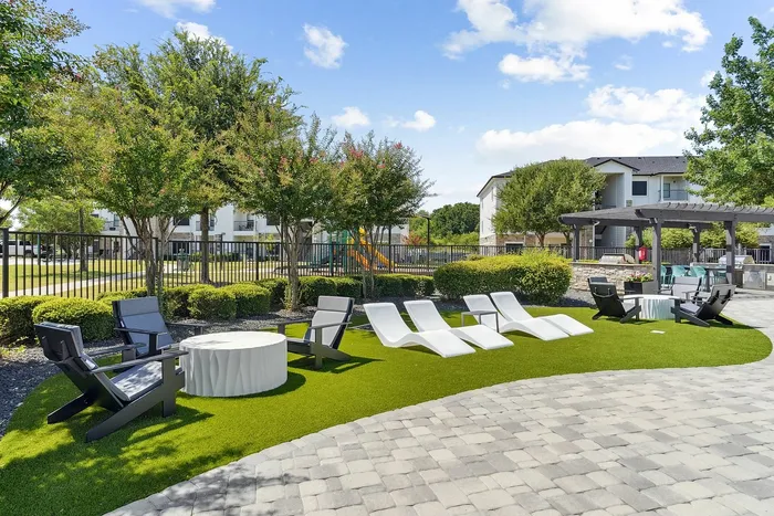 Inviting outdoor community space featuring modern lounge chairs on lush green lawn, surrounded by manicured trees and a stylish pavilion. Perfect for relaxation and social gatherings.