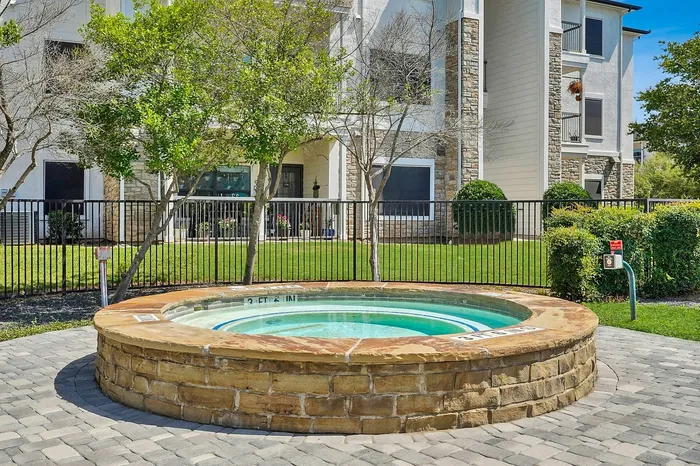 Charming outdoor hot tub surrounded by lush greenery and elegant stonework in a serene apartment setting.