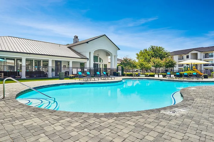 Inviting outdoor pool area with modern lounge chairs, surrounded by elegant architecture and lush greenery under a vibrant blue sky.