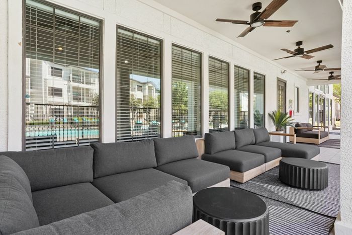 Chic outdoor lounge area with modern gray sofas, round black tables, and ceiling fans, overlooking a scenic poolside view.