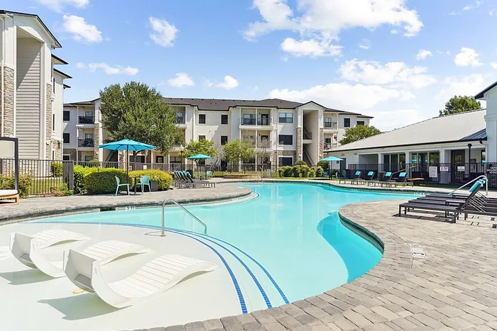 Luxurious apartment featuring a resort-style pool with elegant lounge chairs, surrounded by modern buildings and vibrant landscaping.
