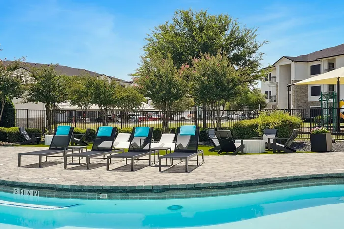 Inviting poolside retreat with stylish lounge chairs, lush greenery, and modern apartment buildings in the background, perfect for relaxation and leisure.