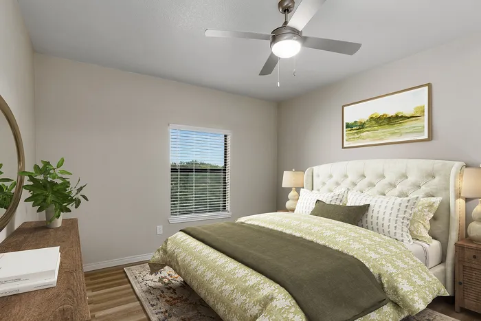 Elegant bedroom boasting a plush upholstered bed with floral bedding, stylish wooden dresser, and modern ceiling fan. Bright natural light streams through the window, highlighting serene artwork and cozy ambiance.