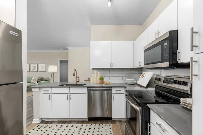 Modern kitchen with sleek white cabinets, stainless steel appliances, and an elegant open view into a cozy living room with stylish decor.