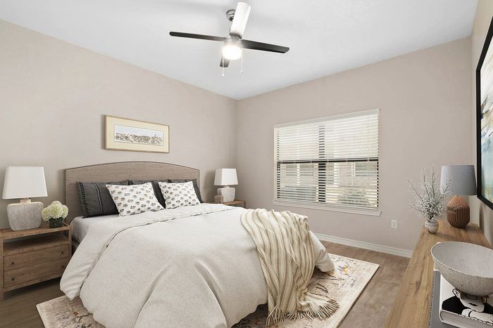 Inviting bedroom with neutral decor, featuring a cozy bed with patterned pillows, stylish nightstands, and chic artwork, illuminated by natural light through large windows.