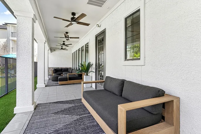 Bright and modern outdoor patio with stylish gray seating, overhead fans, and lush green views.