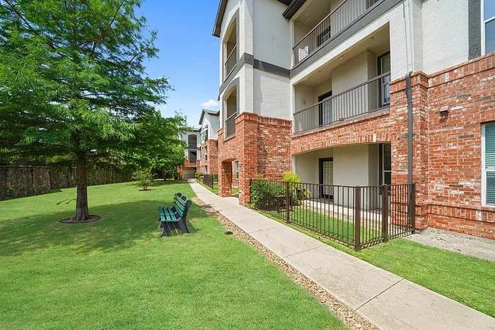 Charming brick apartment complex with lush green landscaping and serene walking paths.