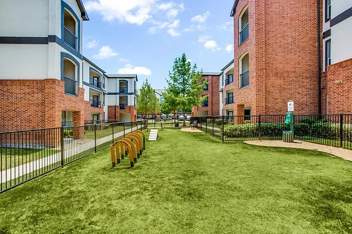 Charming modern apartment complex with red brick exterior and lush green courtyard, perfect for leisurely strolls and outdoor activities.
