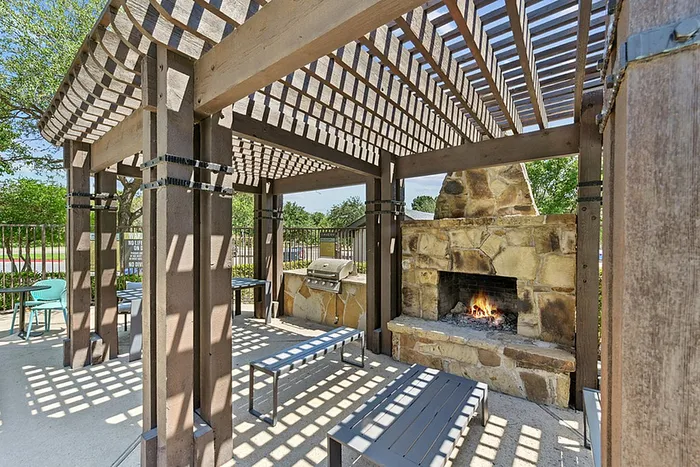 Charming outdoor pergola with a cozy stone fireplace and modern seating area, perfect for relaxing and entertaining.