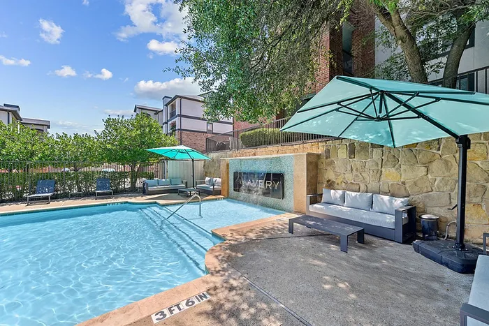 Charming apartment community pool area with inviting lounge chairs, elegant umbrellas, and a serene waterfall feature, perfect for relaxation and leisure.