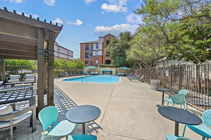 Inviting outdoor pool area with stylish seating, lush greenery, and modern apartment backdrop.
