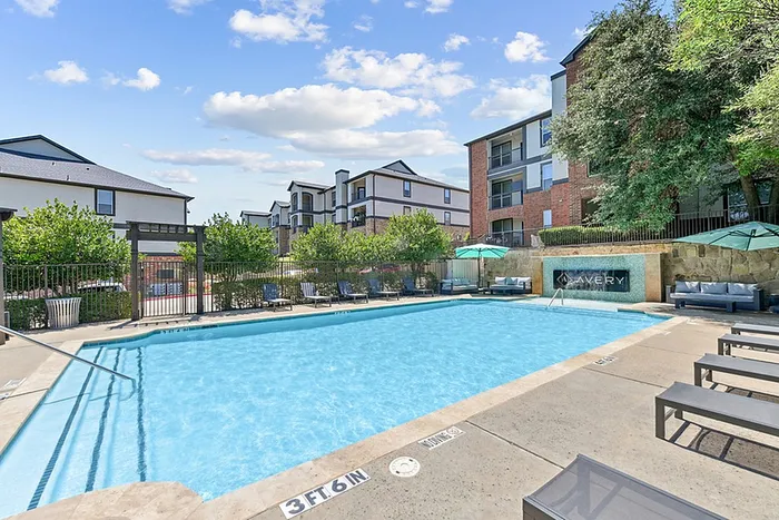 Inviting apartment complex featuring a sparkling outdoor pool surrounded by stylish loungers and lush greenery for a luxurious living experience.