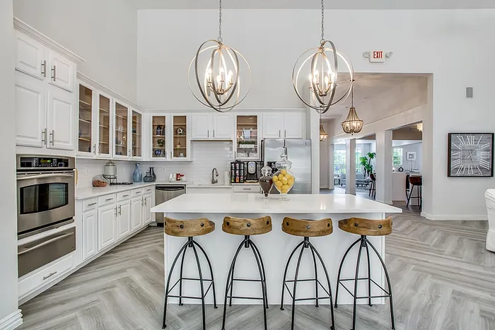 Elegant kitchen with modern white cabinets, stainless steel appliances, and stylish pendant lighting over a spacious island with wooden stools.