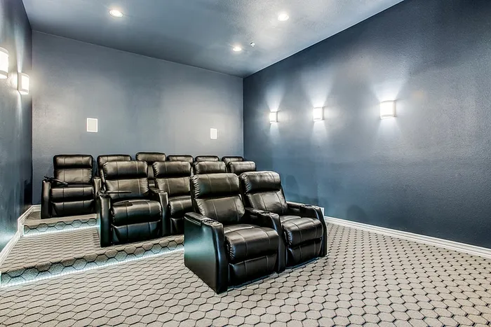Luxurious home theater with comfortable black leather recliners and modern wall lighting for an immersive entertainment experience.