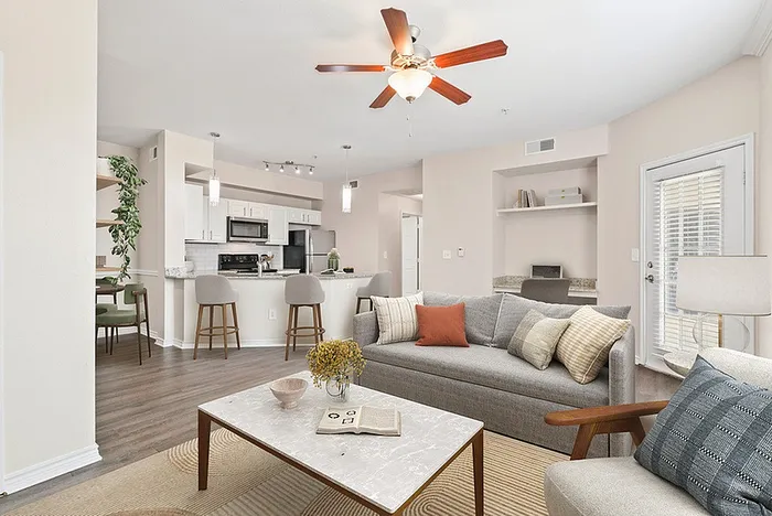 Bright open-concept living room with cozy grey sofa, modern kitchen, and stylish dining area, perfect for entertaining.