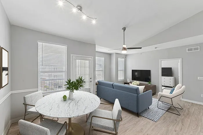 Bright and modern living space featuring an open-concept design with a sleek marble dining table, comfortable seating area, and wall-mounted TV, ideal for relaxation and entertaining.