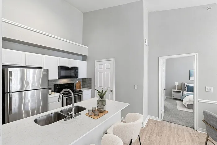 Modern kitchen with sleek stainless steel appliances, marble countertop, and view into cozy bedroom, enhancing open-concept living.