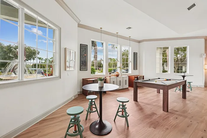 Bright game room with large windows, elegant wood flooring, modern décor, pool table, and inviting seating area.