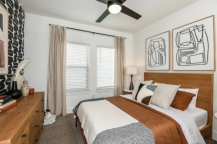 Inviting bedroom with modern decor, featuring a cozy bed, stylish abstract art, and natural light from large windows.