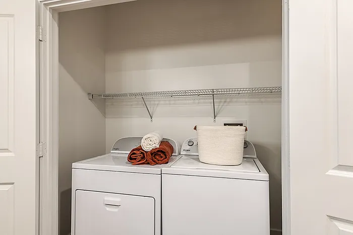 Bright laundry closet featuring a fill-size washer and dryer, accented with cozy towels and a chic storage basket.