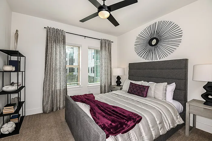 Elegant bedroom featuring a plush, grey upholstered bed with vibrant decor, modern art, and ample natural light.