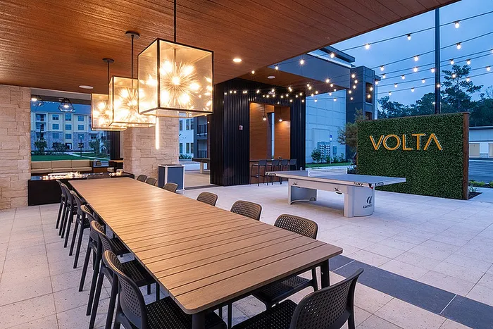 Elegant outdoor lounge area at Volta, featuring modern lighting, ample seating, a fire pit, and a ping-pong table under a stylish wooden canopy.