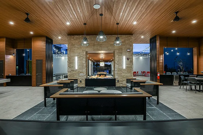 Luxurious lounge area with modern lighting, stylish wooden ceiling, a fire pit, and sleek stone accents, perfect for entertainment and relaxation.