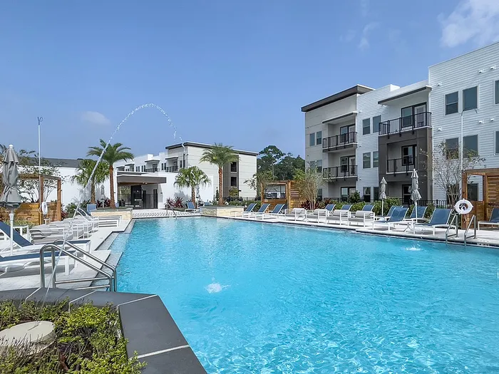Luxurious apartment community featuring a stunning swimming pool, modern buildings, and lush palm trees under a clear blue sky.