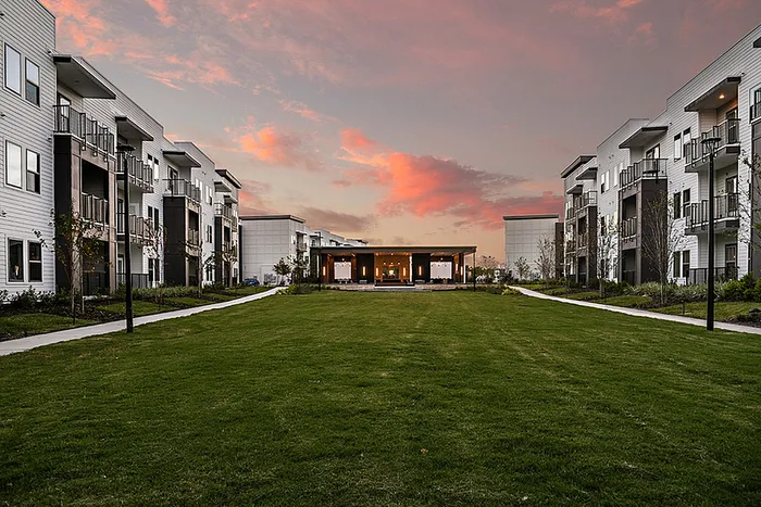 Charming apartment community featuring modern architecture and a spacious green courtyard under a picturesque sunset sky.