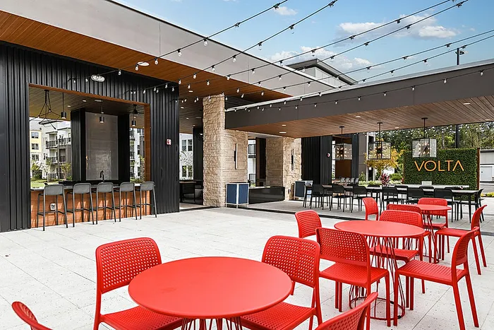 Chic outdoor lounge at Volta featuring vibrant red seating, modern bar area, and sleek string lights under a sunny sky.