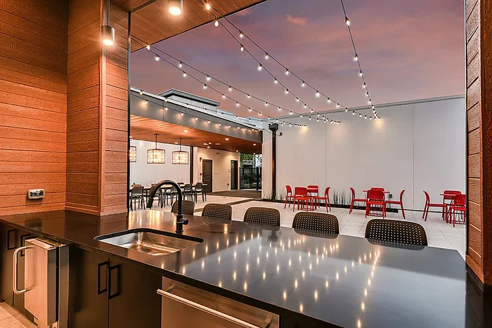 Luxurious outdoor kitchen with sleek countertops and ambient lighting, featuring a stylish patio with vibrant red seating under twinkling string lights.