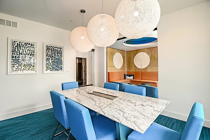 Conference room with a marble table, vibrant blue chairs, modern art, and chic lighting, perfect for entertaining.