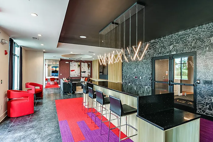 Modern clubhouse space with sleek bar seating, vibrant red accents, and artistic lighting design.