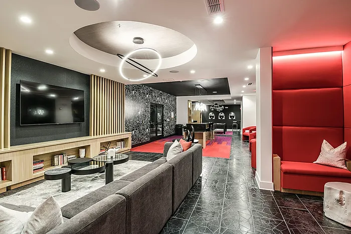 Contemporary clubhouse lounge area featuring sleek furniture, striking red accents, a large TV, and ambient lighting for a modern touch.