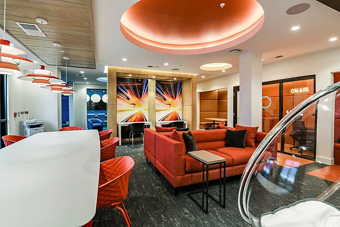 Modern clubhouse lounge area with vibrant red seating, stylish pendant lighting, and dynamic wall art, perfect for relaxation and creativity.
