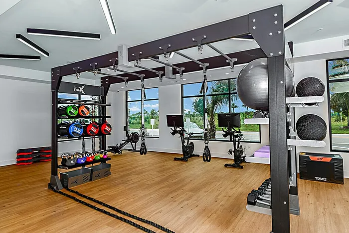 Bright and modern fitness center with state-of-the-art equipment, featuring exercise bikes, kettlebells, and medicine balls, accented by a beautiful view through large windows.