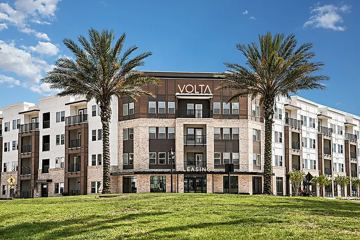 Modern apartment building with a stylish facade, surrounded by lush palm trees under a clear blue sky, offering vibrant community living.