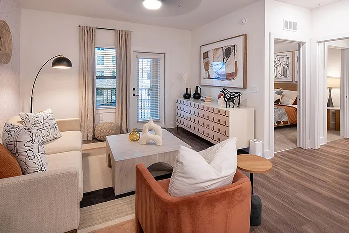 Chic modern living room with cozy seating, stylish décor, and inviting natural light leading to a tranquil bedroom.