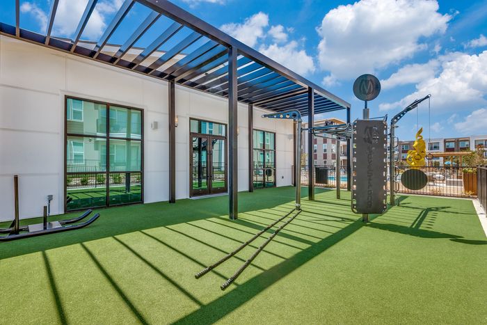 Modern outdoor fitness area with sleek exercise equipment and vibrant green turf under a stylish pergola on a sunny day.